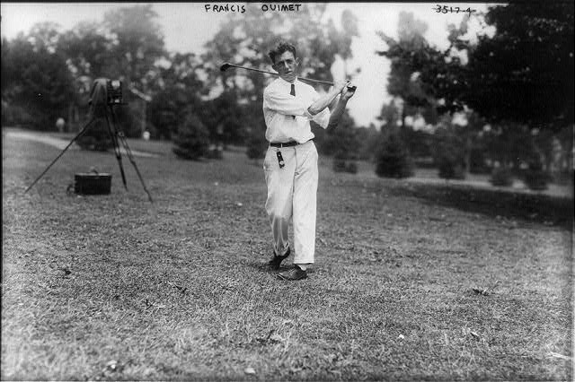 Francis Ouimet at the finish of a swing on a fairway, with a plate camera on a tripod behind him, 1913